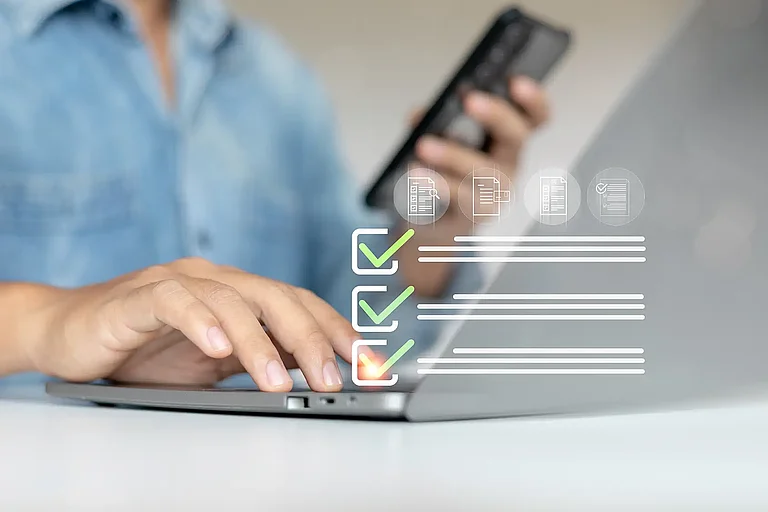 A person is using a laptop and holding a smartphone while interacting with a virtual checklist. Concept of digital task management, form submission and productivity tools.