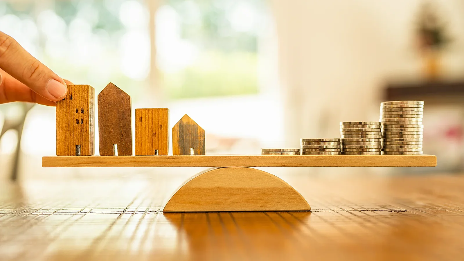 A wooden house and coins are stacked on a scale pan. Money management, financial planning, time value of money. Real estate agents and brokers offer home design concepts.