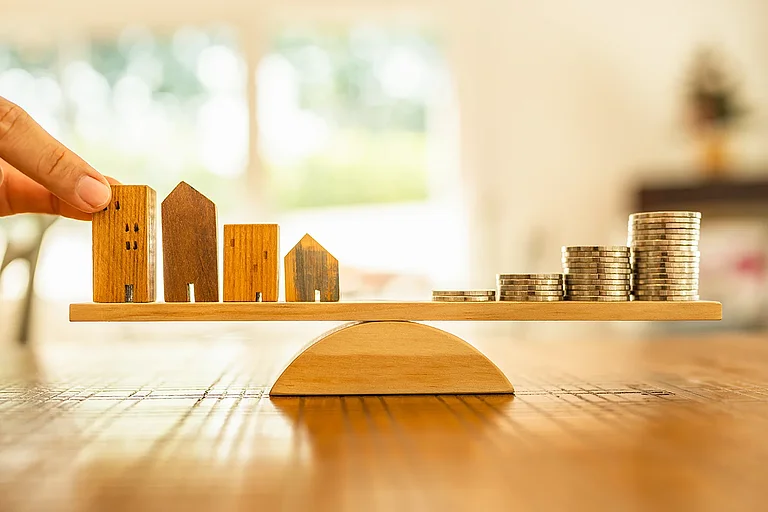 A wooden house and coins are stacked on a scale pan. Money management, financial planning, time value of money. Real estate agents and brokers offer home design concepts.
