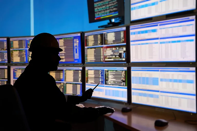 SCADA system in the central heating process. Silhouette of an operator analyzing data on multiple monitors—to ensure optimal performance and safety in industrial automation systems.